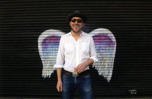 Unidentified man smoking a cigarette posing in front of a mural depicting angel wings