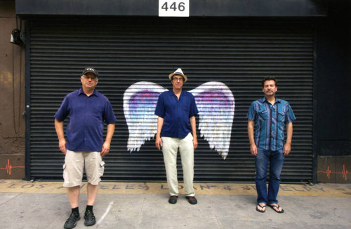 Three unidentified men posing in front of a mural depicting angel wings