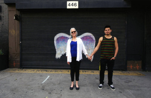 Unidentified man and woman holding hands and posing in front of a mural depicting angel wings