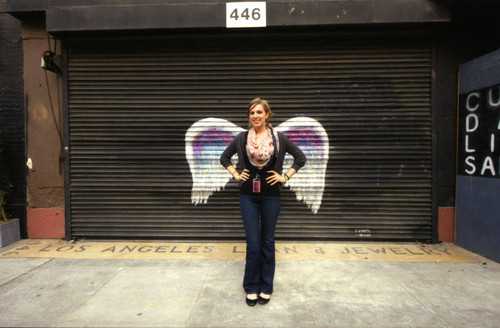 Unidentified woman wearing a scarf posing in front of a mural depicting angel wings