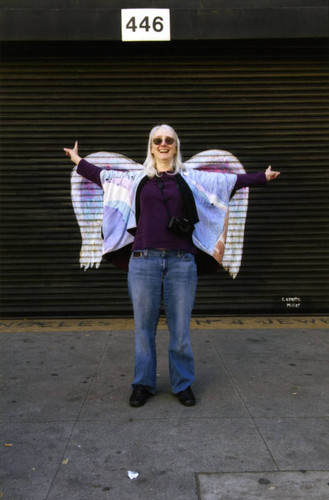 Unidentified woman with arms outstretched posing in front of a mural depicting angel wings