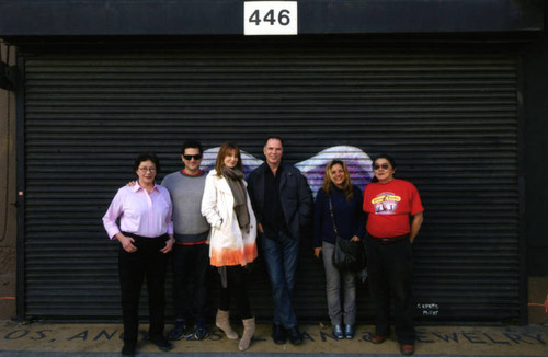 A group of six people posing in front of a mural depicting angel wings