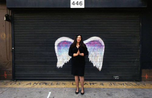 Unidentified woman in a black dress posing in front of a mural depicting angel wings