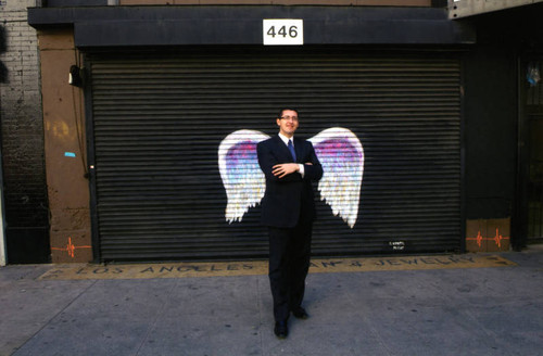 Unidentified man in suit posing in front of a mural depicting angel wings