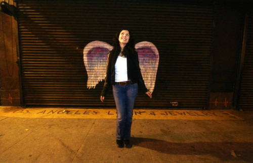 Unidentified woman posing in front of a mural depicting angel wings