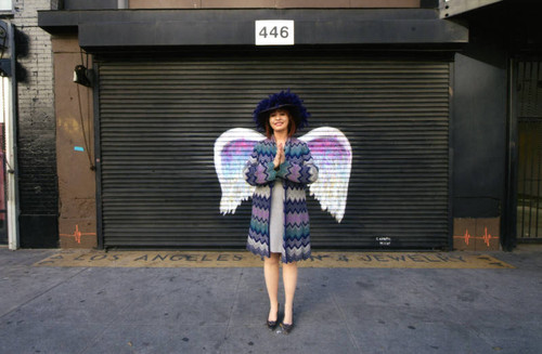 Journalist Patt Morrison posing in front of a mural depicting angel wings