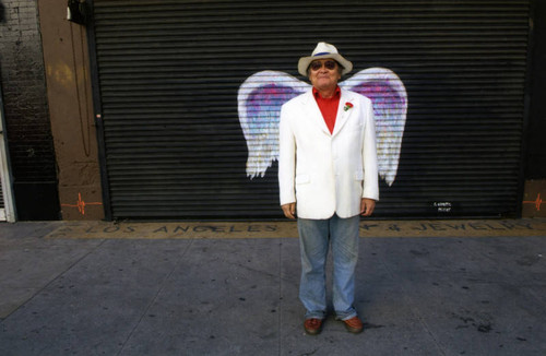 Thomas "T.K." Nagano posing in front of a mural depicting angel wings