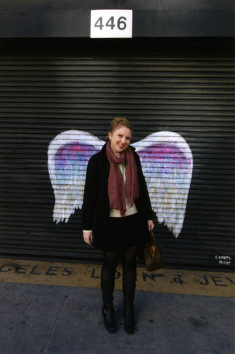 Katie Dunham, communications consultant, posing in front of a mural depicting angel wings