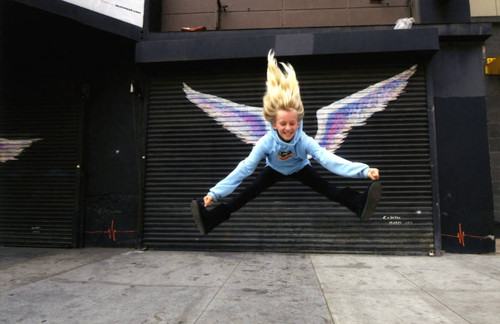 Unidentified child in a light blue hoodie jumping in front of a mural depicting angel wings