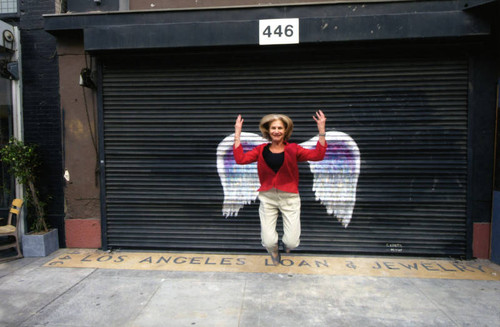 Louise Steinman jumping in front of a mural depicting angel wings