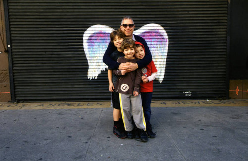 Unidentified man with three children posing in front of a mural depicting angel wings