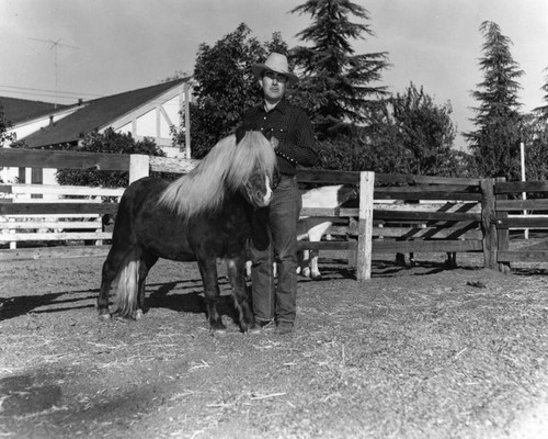 Cowhand poses a Shetland pony