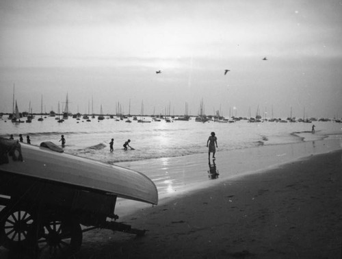 Yachts, a boat, a wagon, and bathers share the ocean