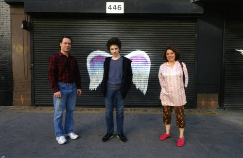 Unidentified group of three people posing in front of a mural depicting angel wings