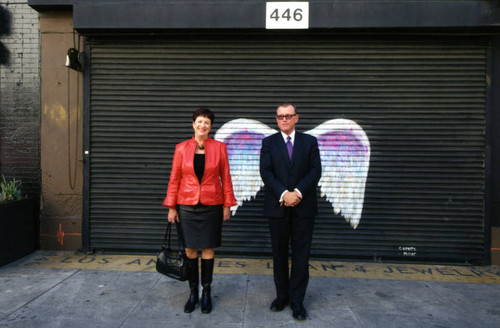 Carol Schatz and Hal Bastian posing in front of a mural depicting angel wings