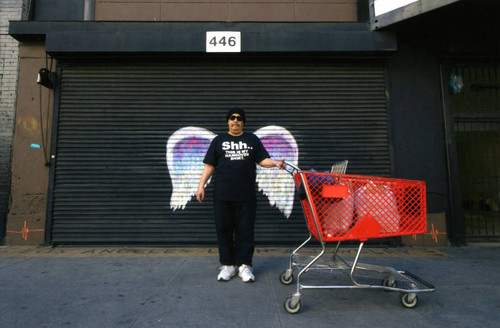 Unidentified man in sunglasses with a shopping cart posing in front of a mural depicting angel wings