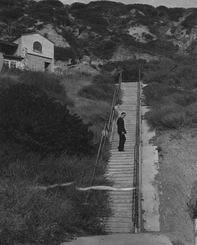 It was surmised that Thelma Todd may have walked up these steps which lead from her seaside cafe to the road on which the garage where she was found dead was located. Here a man stands part of the way up the steps.; The three-story, 15,000-square-foot Spanish style structure where the murder took place was located at 17575 Pacific Coast Highway in Pacific Palisades. In the early 1930s, this structure housed a restaurant on the ground floor owned by actress Thelma Todd and her partner Roland West. The duo also held parties in their private nightclub named Joya's, located on the second story near her personal apartment. At the time Todd owned the building, the hexagonal-shaped, third-floor included a dance floor and bandstand., which was famous for its Joya's barbequed steaks.