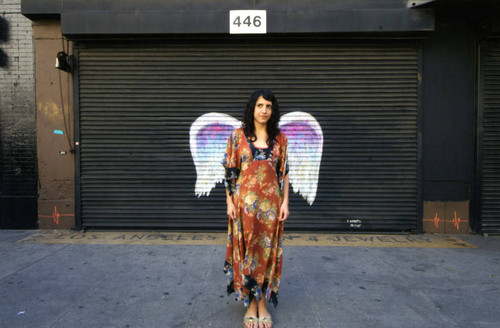 Unidentified woman in a long dress posing in front of a mural depicting angel wings