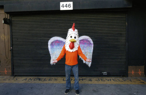 Unidentified person in Chicken Boy costume posing in front of a mural depicting angel wings