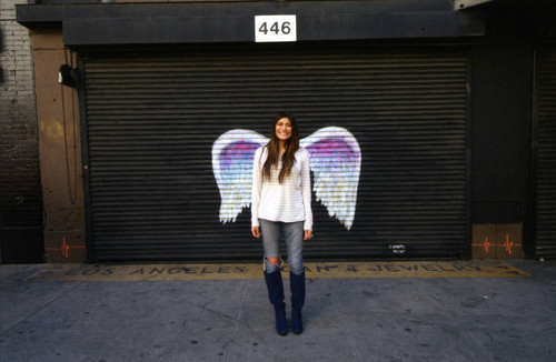 Unidentified woman posing in front of a mural depicting angel wings