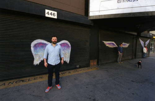 Unidentified man in a white shirt posing in front of a mural depicting angel wings