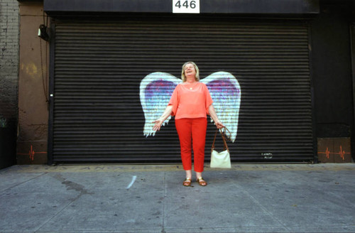 Unidentified woman in red pants posing in front of a mural depicting angel wings