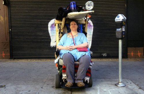 Unidentified woman in a wheelchair posing in front of a mural depicting angel wings