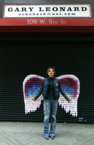 Colette Miller posing in front of a mural depicting angel wings