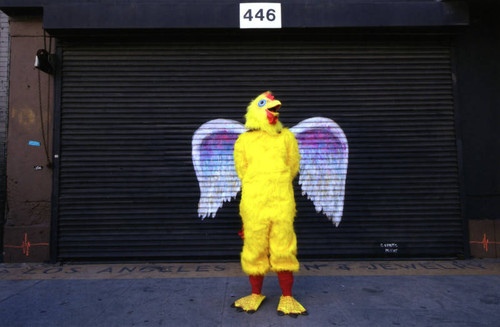 Unidentified person in a chicken costume posing in front of a mural depicting angel wings