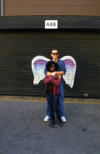 Unidentified man and woman posing in front of a mural depicting angel wings