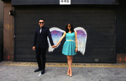 Unidentified man and woman holding hands and posing in front of a mural depicting angel wings