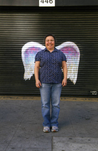 Unidentified woman posing in front of a mural depicting angel wings