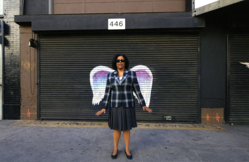 Jan Perry posing in front of a mural depicting angel wings