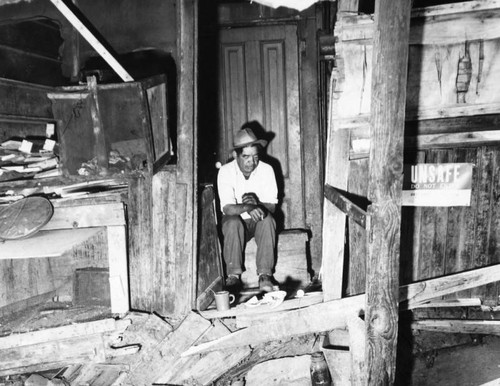 Man sits in doorway of his dilapidated home