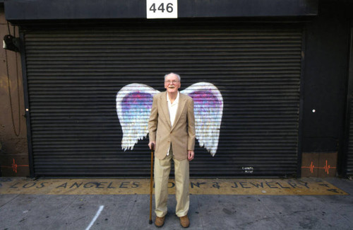 Unidentified man with a cane posing in front of a mural depicting angel wings