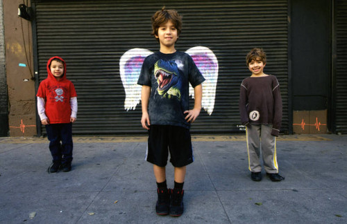 Three unidentified children posing in front of a mural depicting angel wings