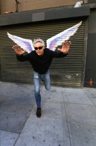 Unidentified man posing on one leg in front of a mural depicting angel wings