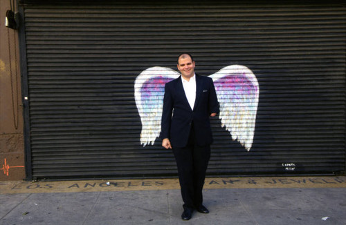 Unidentified man in suit smiling and posing in front of a mural depicting angel wings