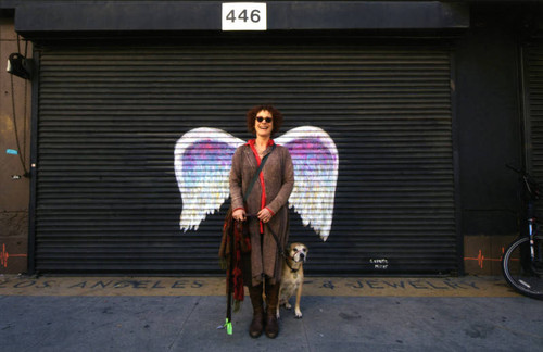 Unidentified woman with dog posing in front of a mural depicting angel wings