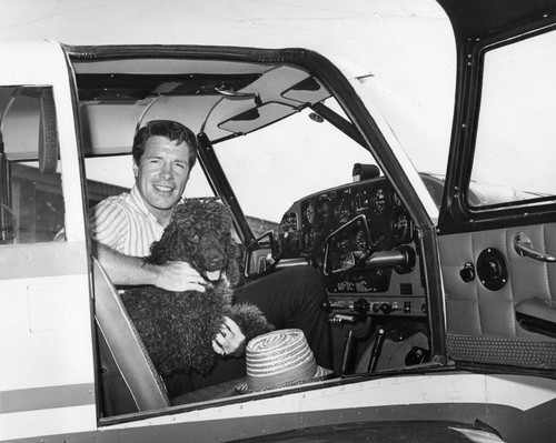 Actor Robert Horton sitting in an airplane with poodle