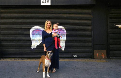 Unidentified woman with child and dog posing in front of a mural depicting angel wings