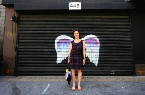 Unidentified woman in a dress posing in front of a mural depicting angel wings