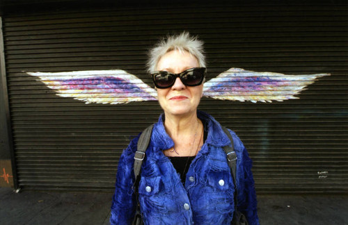 Unidentified woman in sunglasses posing in front of a mural depicting angel wings