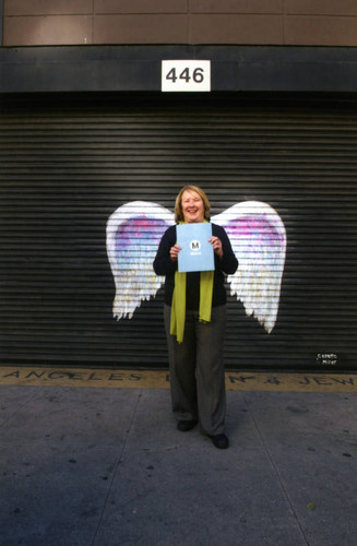 Unidentified woman holding a Metro document posing in front of a mural depicting angel wings