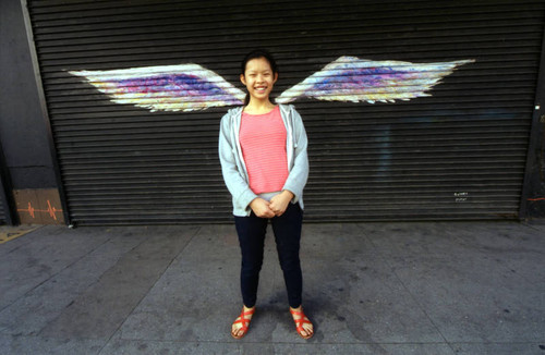 Unidentified woman posing in front of a mural depicting angel wings