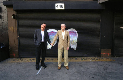 Two unidentified men holding hands in front of a mural depicting angel wings