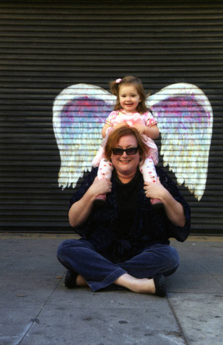 Jessica Wethington McLean seated with child posing in front of a mural depicting angel wings