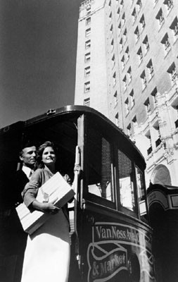 [Two unidentified people on a cable car in front of the Mark Hopkins Hotel]