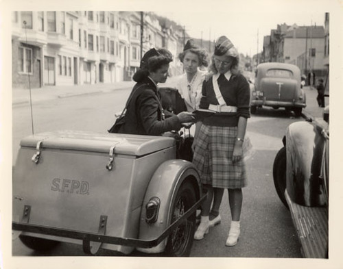 [Patrolwoman sits on her three wheeled motorcycle while talking with two girls]