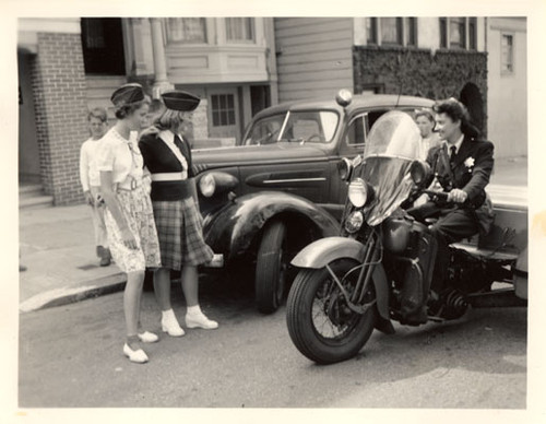 [Patrolwoman sits on her three wheeled motorcycle while talking with young people]